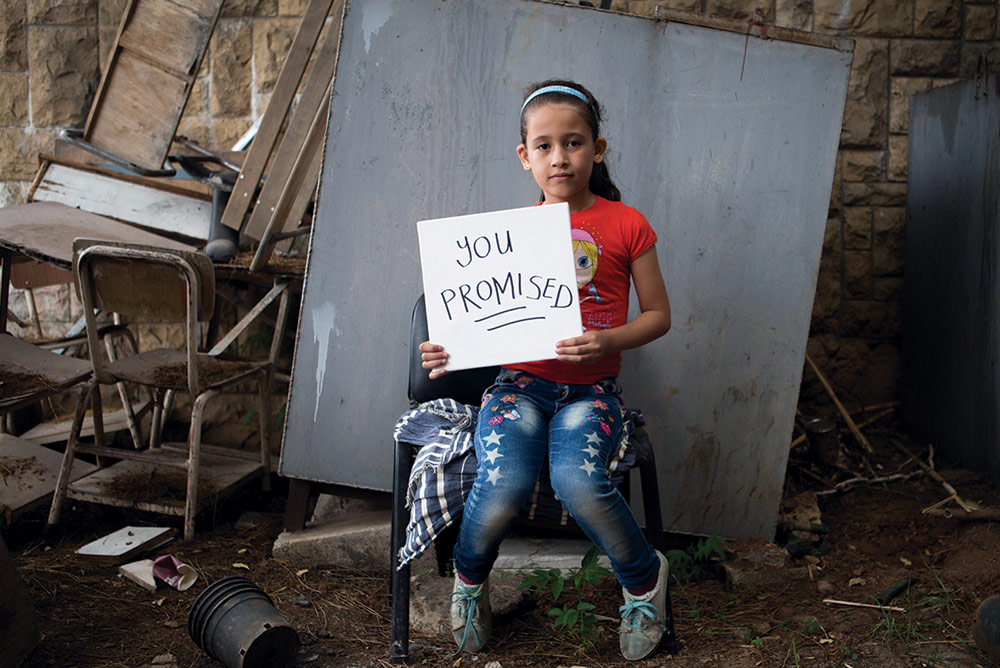 refugee child holding "You Promised" sign