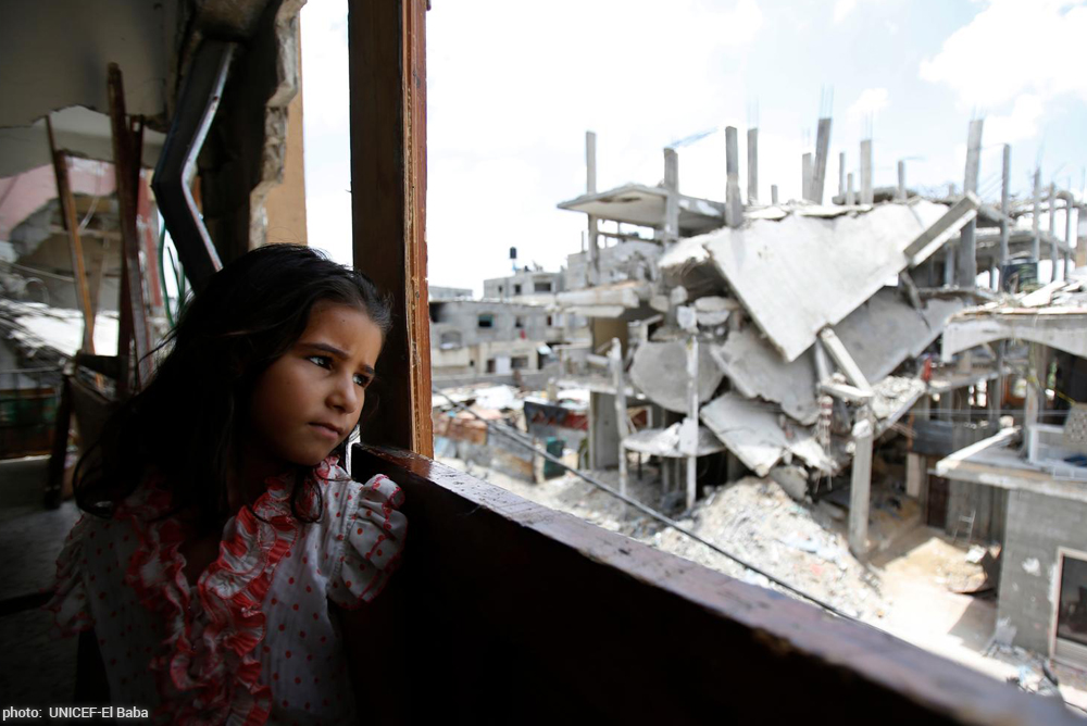 girl looks out window at bombed street